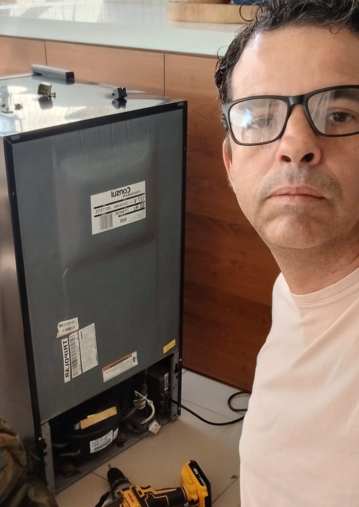 Rafael durante a manutenção de uma adega, com o compartimento do compressor aberto e as ferramentas ao lado