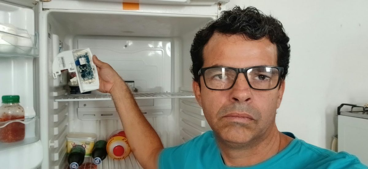 Rafael fazendo a manutenção de uma geladeira, segurando a placa eletrônica retirada do aparelho