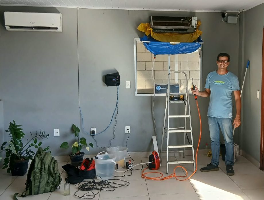 Rafael durante a higienização de um ar-condicionado split, com o aparelho aberto, a bolsa coletora instalada e a lavadora ao lado