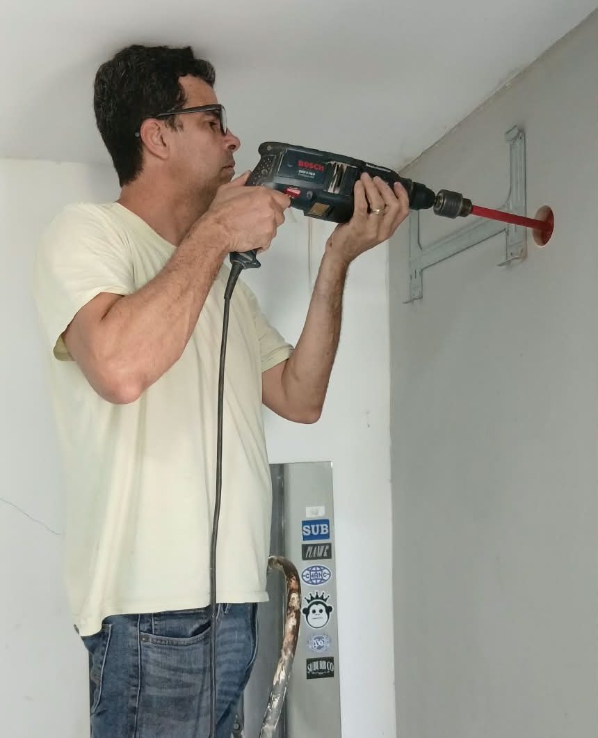 Rafael furando a parede para a passagem da tubulação do ar-condicionado, com o suporte já fixado